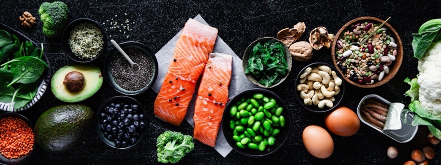 Nährstoffreiche Lebensmittel auf dunklem Stein — Lachs, Avocado, Spinat, Hülsenfrüchte, Nüsse und Eier