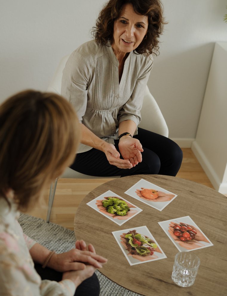 Isabel Kratzenberg zeigt einer Klientin anhand von Karten passende Portionsgrößen für Gemüse und Obst